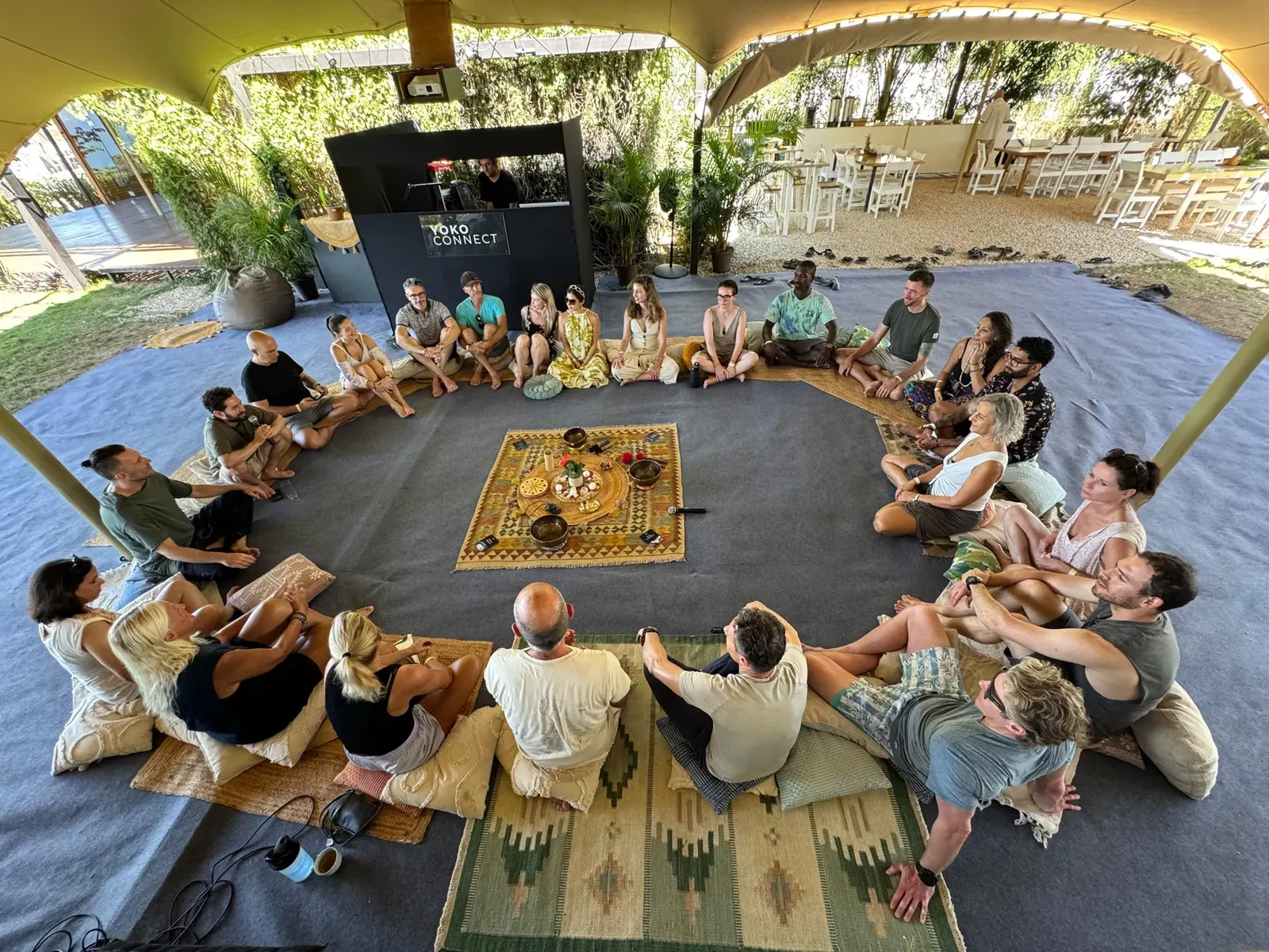 People sitting in a circle on cushions inside a large tent