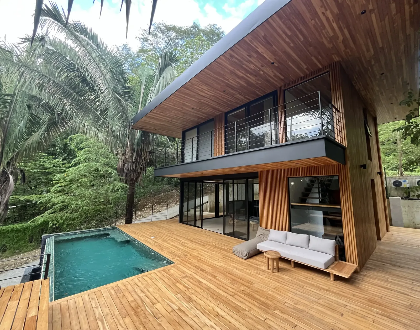 Wood-clad two-storey villa with a pool and a wide teak deck among palms
