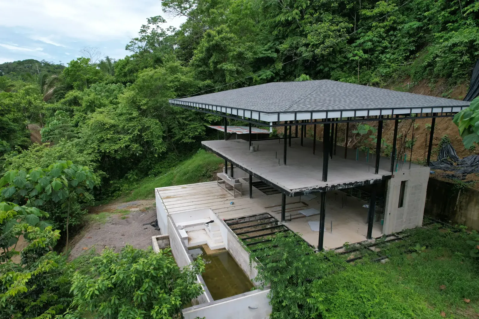 Drone view of a half-built two-storey villa with a pool among trees